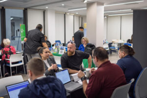 A man and a woman attending the event sit next to each other and across the consultation table from Planning and Zoning, Finance and Building Department staff while reviewing documents during Business-Ready Day. Additional resource tables and participants are visible in the background.