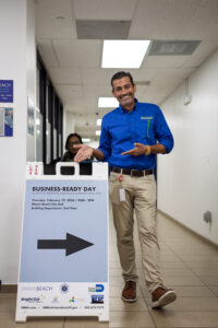 An Economic Development staff member stands in a hallway next to a Business Ready Day directional sign with an arrow pointing toward the event location.