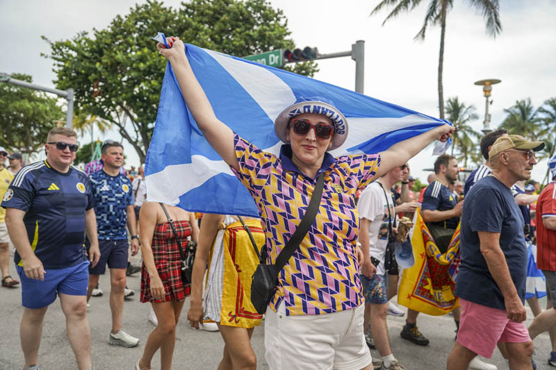 woman holding flag of Scottland as others march behind her
