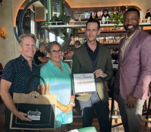 Steven Anthony, Economic Development Director, presenting a Welcome Certificate to Ezio General Manager, David Beaty, accompanied by Commissioner Tanya Bhatt and David Sexton