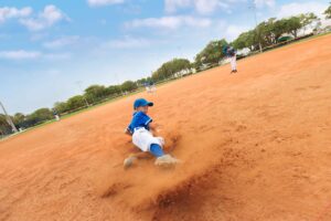boy in baseball uniform sliding in dirt on the baseball infield