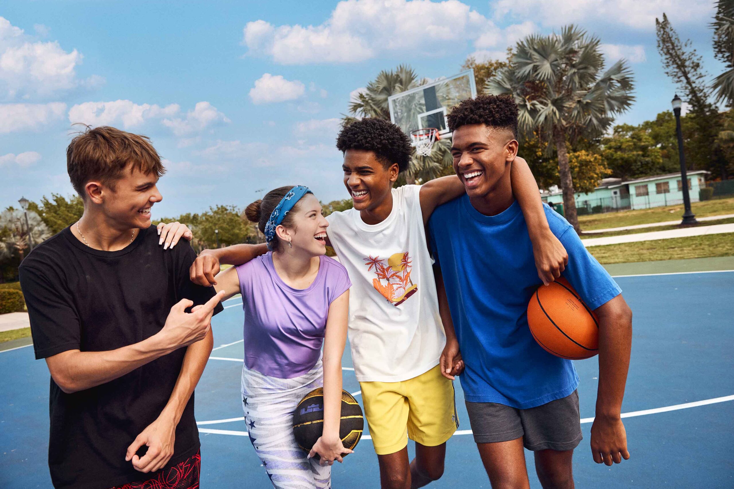 4 kids with arms around each other's shoulders smiling, boy on right end is holding a basketball