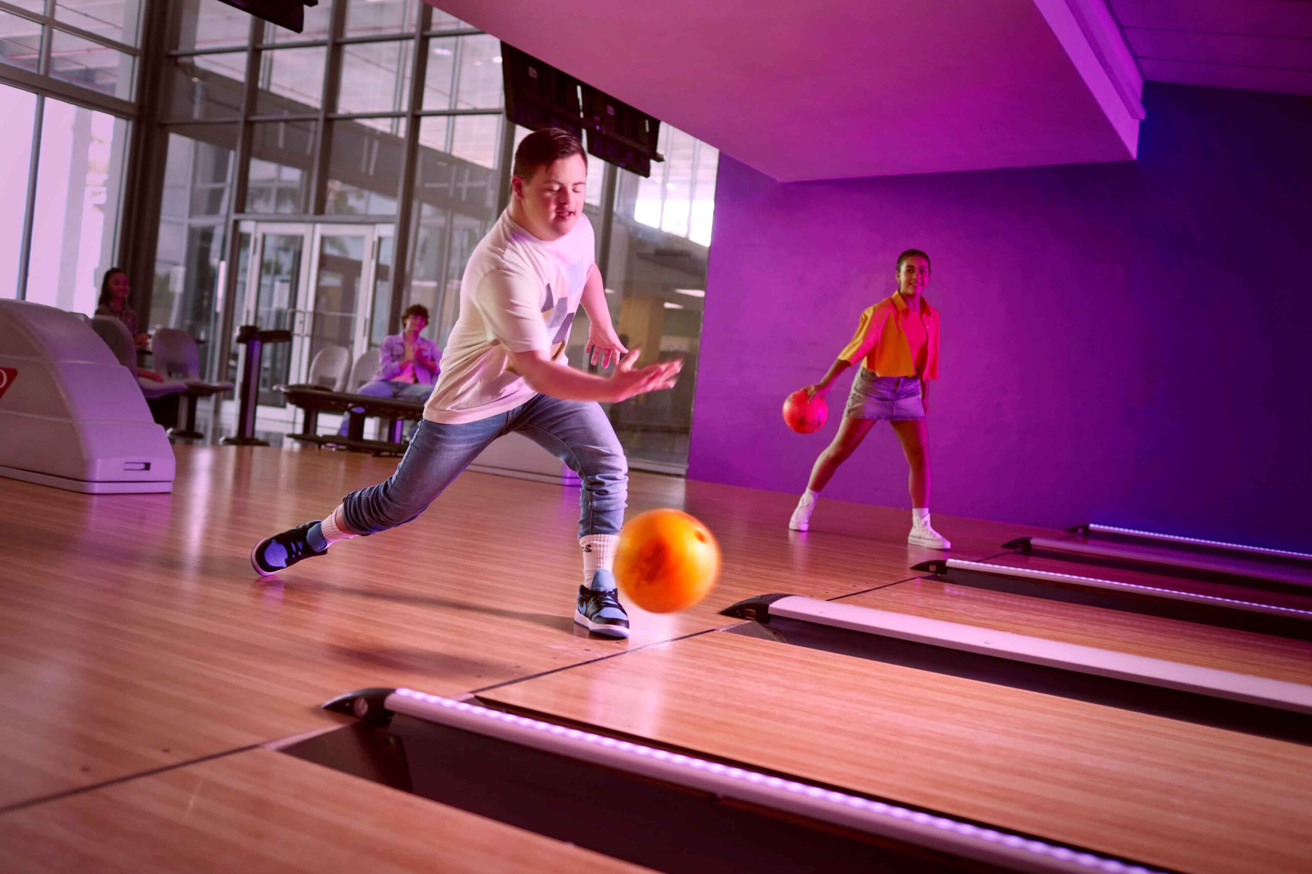 boy bowling in front lane as girl bowls in lane behind him