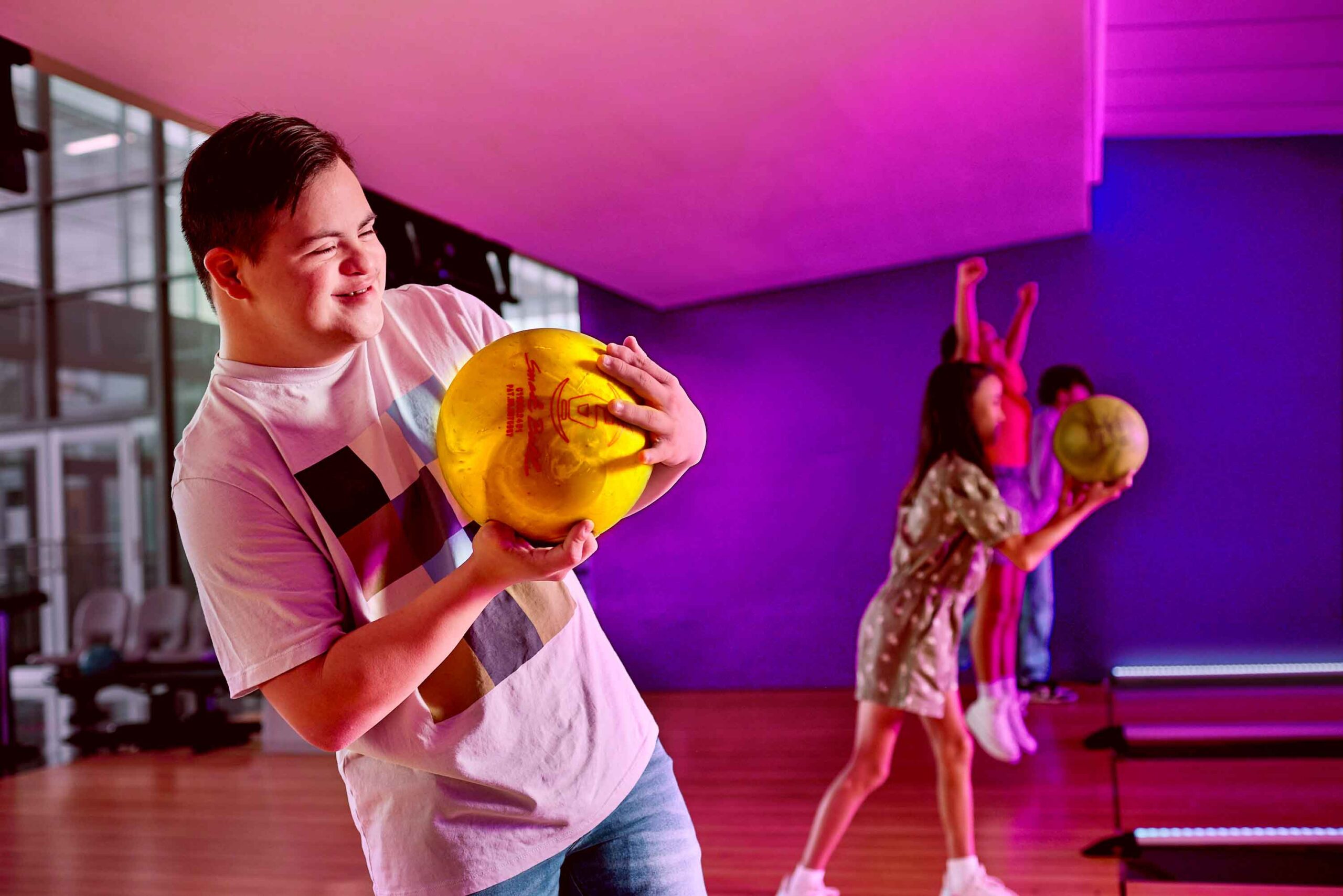 boy holding bowling ball as girl bowls in background