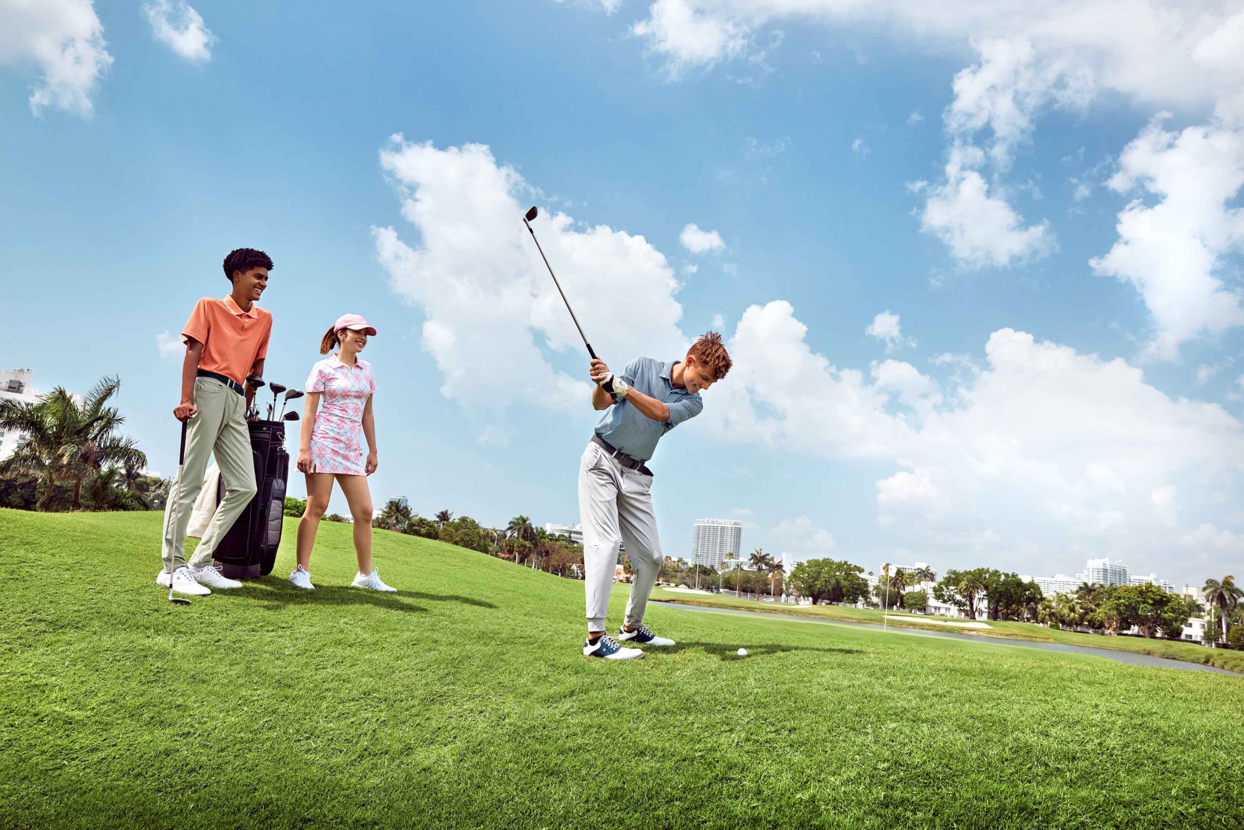 boy swinging golf club as boy and girl watch from the side with their golf equipment