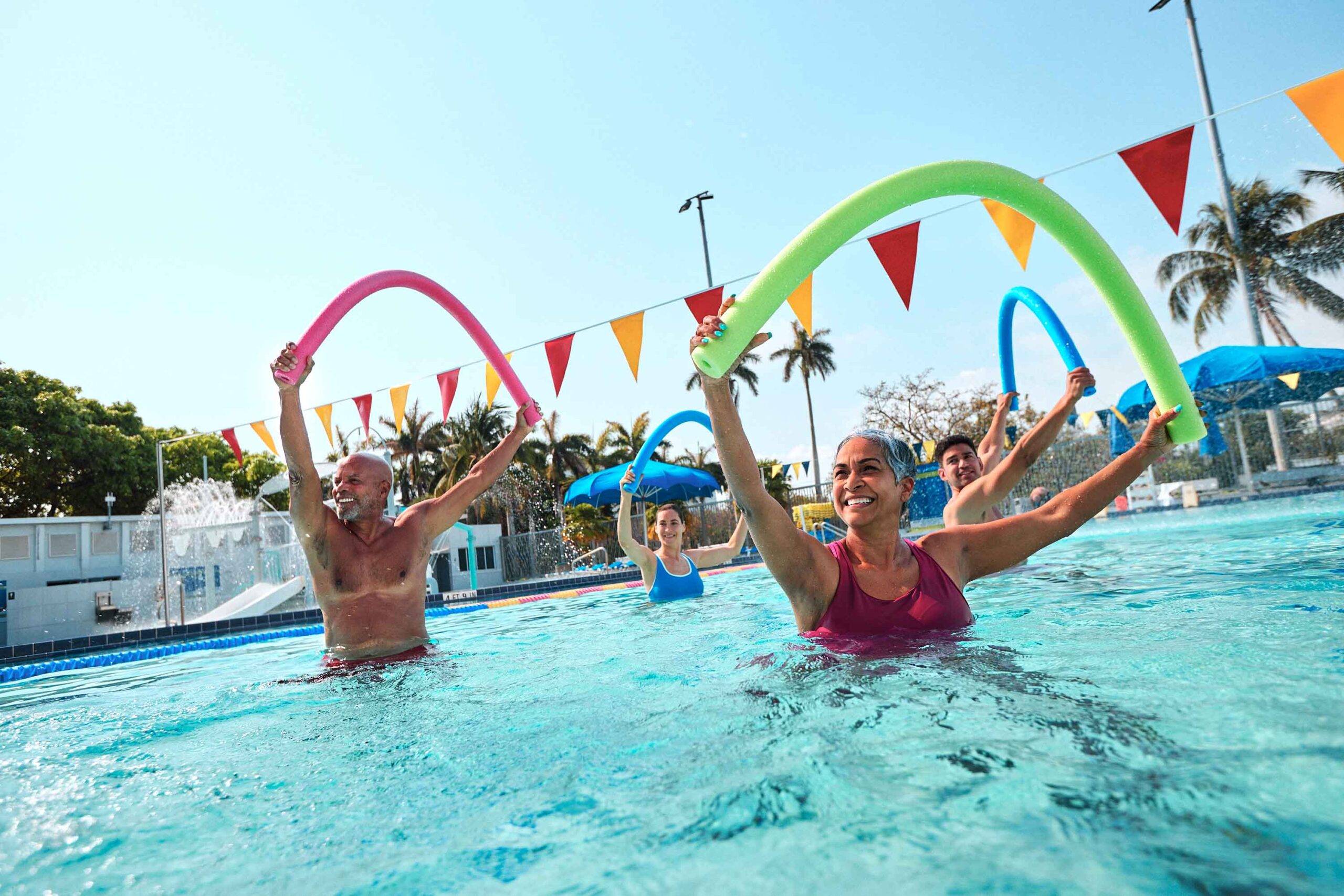 people doing group class in pool holding pool noodles
