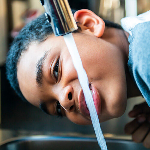 boy drinking water out of a faucet